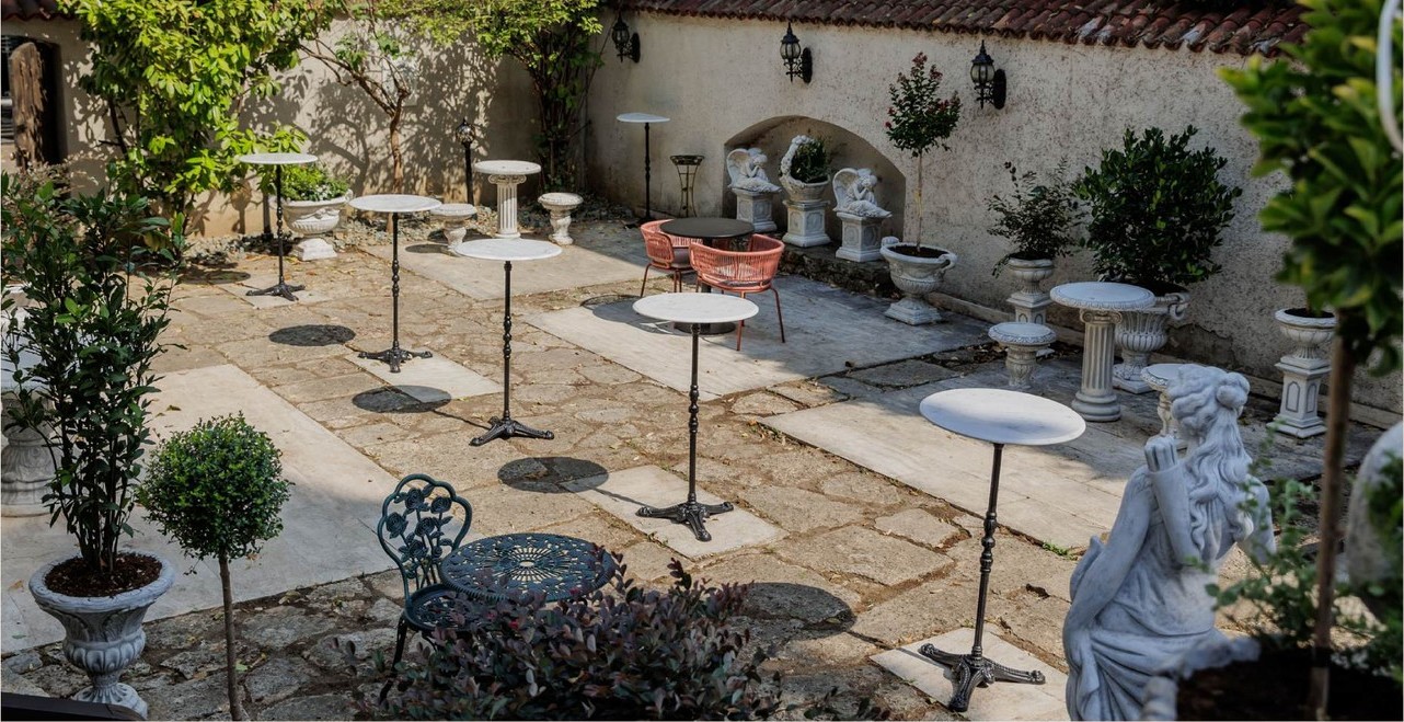 The inner courtyard of Vila Tătărescu set for a cocktail reception: high tables, wrought-iron chairs, statues and plants